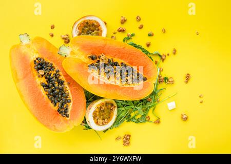 Papaya, Passionsfrucht, Rucola und Müsli auf gelbem Hintergrund. Scheiben von süßer Papaya, Passionsfrucht, Rucola umgeben von Granola Flocken auf Gelb Stockfoto