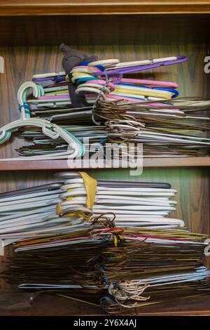 Zusammengebundene Bündel aus verschiedenen Metall- und Kunststoffbügeln auf Holzregalen im Bücherregal im Gebrauchtwarengeschäft. Stockfoto