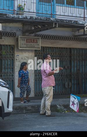 Balikpapan, Indonesien - 26. Juni 2024. Mit einem bunten Drachen in der Hand steht der Vater neben dem Bürgersteig, sein Sohn an seiner Seite. Stockfoto