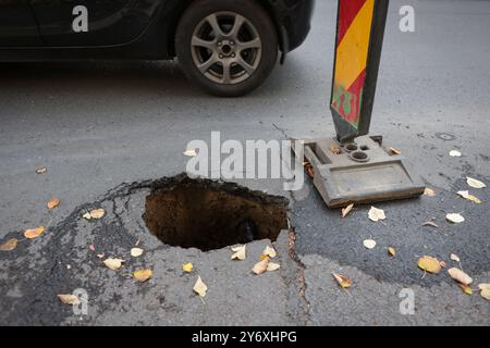 Details mit einem großen Schlagloch mitten auf einer asphaltierten Straße mit vorbeifahrenden Autos Stockfoto