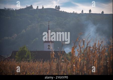 Eine Rauchwolke weht in den Himmel und erhebt sich über einem malerischen ländlichen Dorf, eingebettet in sanfte Hügel Stockfoto