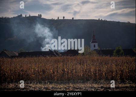 Eine Rauchwolke weht in den Himmel und erhebt sich über einem malerischen ländlichen Dorf, eingebettet in sanfte Hügel Stockfoto