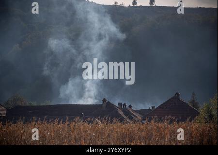 Eine Rauchwolke weht in den Himmel und erhebt sich über einem malerischen ländlichen Dorf, eingebettet in sanfte Hügel Stockfoto