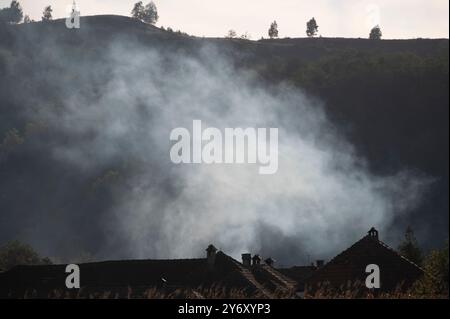 Eine Rauchwolke weht in den Himmel und erhebt sich über einem malerischen ländlichen Dorf, eingebettet in sanfte Hügel Stockfoto