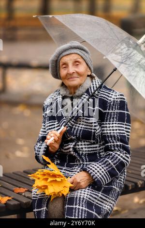 Ältere Frau im grauen Mantel mit Regenschirm im Herbst Stockfoto