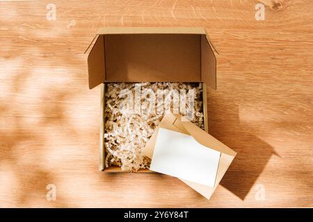 Öffnen Sie den Karton, der mit geschreddertem Papier und einer leeren Karte auf einer Holzoberfläche gefüllt ist Stockfoto