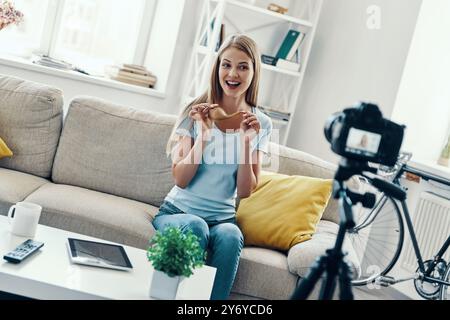 Schöne junge Frau lächelt und zeigt ihre Haarspitzen, während sie zu Hause Social Media Videos macht Stockfoto