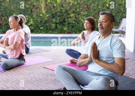 Yoga üben, Seniorenfreunde, die auf Matten am Pool im Freien meditieren, zu Hause Stockfoto