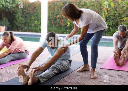 Yoga praktizieren, ältere, vielfältige Freunde, die sich auf Matten unter Anleitung des Lehrers ausstrecken, zu Hause Stockfoto