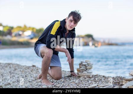 Hübscher junger Mann, der eine Pyramide aus Steinen am Meer baut Stockfoto