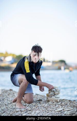 Junger, gutaussehender Mann, der am Meer aus Steinen einen einen Stein baut Stockfoto