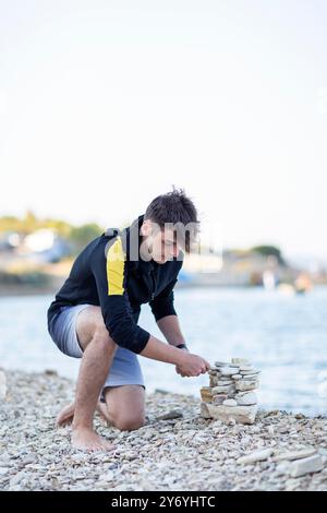 Hübscher junger Mann, der eine Pyramide aus Steinen am Meer baut Stockfoto