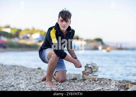Junger, gutaussehender Mann, der am Meer aus Steinen einen einen Stein baut Stockfoto