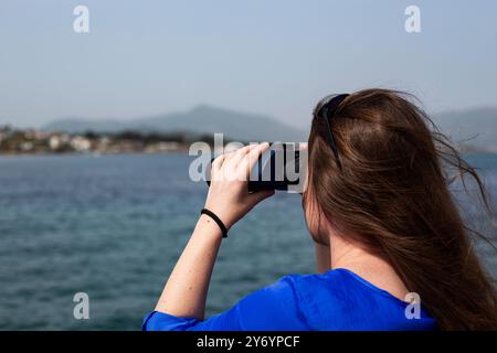 Eine junge Frau mit langen Haaren schaut durch ein Fernglas ins Meer Stockfoto