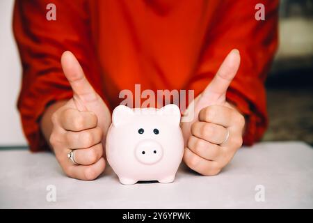 Eine Frau in einer roten Bluse gibt sich neben einer rosa Schweinebank die Daumen hoch Stockfoto