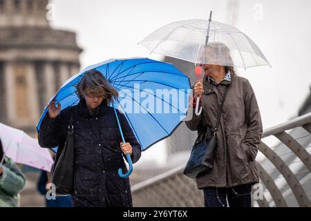 Menschen, die Regenschirme tragen, laufen durch den Regen auf der Millennium Bridge in London, nachdem Teile Englands in den frühen Morgenstunden von starkem Regen und Überschwemmungen heimgesucht wurden. Bilddatum: Freitag, 27. September 2024. Stockfoto