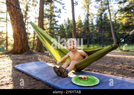 Ein Kleinkind lächelt, während er in einer Hängematte beim Camping spielt. Stockfoto