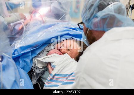 Mutter lächelt, während sie ihr Baby nach dem C-Schnitt auf dem Operationstisch trifft Stockfoto