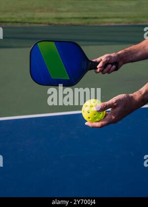 Nahaufnahme der Hand, die Pickleball-Paddel und -Ball auf dem Platz im Freien hält. Stockfoto