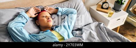 Eine junge Frau liegt im Bett, ihre Finger dehnen sich hinter ihrem Kopf, während sie ihren Tag betrachtet. Stockfoto