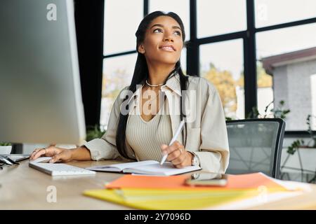 Eine junge, schöne Frau sitzt an ihrem Schreibtisch, taucht in ihre Arbeit ein, während sie detaillierte Notizen macht. Stockfoto