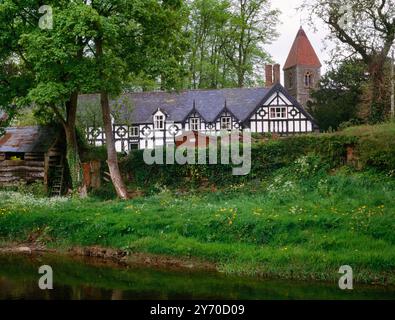Blick auf NE über den Fluss Rhiw & Church Terrace schwarz-weiße Häuser zum 19. Turm der St. Beuno's Church, Berriew (aber Rhiew), Powys, Wales, Großbritannien. Stockfoto