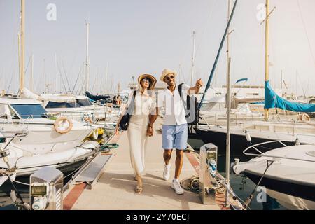 Ein fröhliches Paar, das einen sonnigen Tag am Yachthafen genießt und entlang des Docks von Booten spaziert. Stockfoto