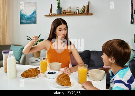 Ein kleiner Junge mit Hörstörungen frühstückt mit seiner aufmerksamen Mutter und teilt ein Lächeln. Stockfoto