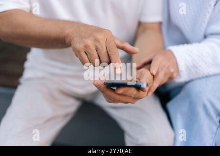 Nahaufnahme: Ein Foto von älteren verheirateten Paaren, die ihr Smartphone nutzen, Apps erkunden, mit der Welt in Verbindung bleiben und das digitale Zeitalter im Ruhestand nutzen. Stockfoto