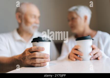 Selektive Fokusaufnahme eines älteren Paares, das gute Zeit miteinander verbringt, Kaffeetassen zum Mitnehmen hält, während es in einem gemütlichen Café ein Gespräch führt Stockfoto