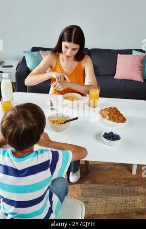 Ein kleiner Junge frühstückt mit seiner aufmerksamen Mutter in gemütlicher Atmosphäre. Stockfoto