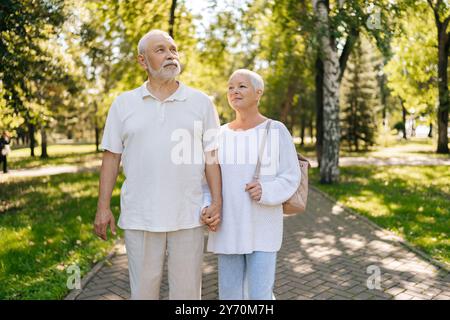 Porträt eines liebevollen Seniorenpaares, das einen gemütlichen Spaziergang durch den grünen Park macht, die Hände miteinander verflochten hält und an sonnigen Sommertagen zärtliche Momente teilt. Stockfoto