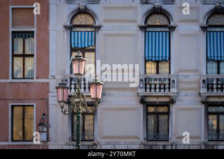 Pinkfarbene venezianische Glaslampen bei Sonnenaufgang. Verzierte traditionelle venezianische pinkfarbene Laterne mit drei Lampen, ein altes Gebäude auf dem Hintergrund. Stockfoto