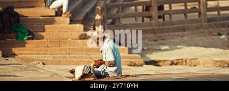 Varanasi, Indien. Der Alte Bettler Zählt Seine Einnahmen. Ein Alter Mann Sitzt Am Ganges Embankment. Der Senior-Mann Zählt Sein Geld. Vormittag Im Heiligen Varanasi Ghats Stockfoto