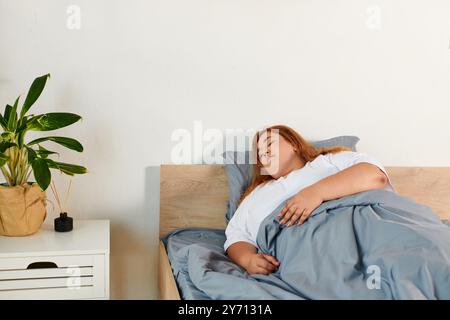 Eine schöne Frau in Übergröße ruht ruhig in ihrem Bett, in weiche Decken gehüllt und strahlt Ruhe aus. Stockfoto