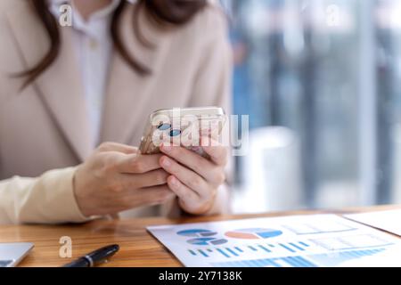 Nahaufnahme der Hände einer jungen Geschäftsfrau, die ihr Telefon hält, um ihre Nachrichten an ihrem Schreibtisch zu überprüfen Stockfoto