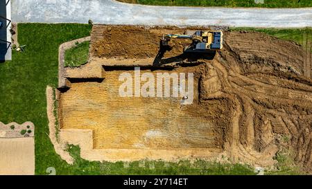 Ein Bagger gräbt sich in den Boden, um ein Fundament für den Bau eines neuen Gebäudes in einer Wohngegend vorzubereiten. Der Bereich ist klar und zeigt die Grundrisse der Baustelle. Stockfoto