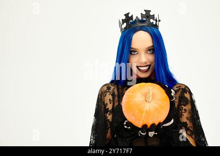 Eine schöne Frau in einem Halloween-Outfit lächelt hell, während sie einen Kürbis hält. Stockfoto