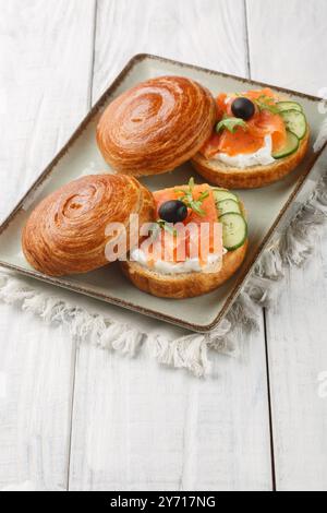 Halbmondbrötchen-Sandwich mit Lachs, Frischkäse, frischen Gurken und Oliven in Nahaufnahme auf einem Teller auf dem Tisch. Vertikal Stockfoto