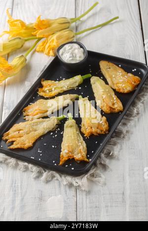 Köstliche frittierte panierte Zucchini-Blüten gefüllt mit Ricotta-Käse in Nahaufnahme auf einem Teller auf dem Tisch. Vertikal Stockfoto