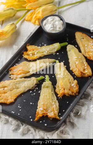Frittierte panierte Zucchini-Blüten mit Ricotta-Käse in Nahaufnahme auf einem Teller auf dem Tisch. Vertikal Stockfoto