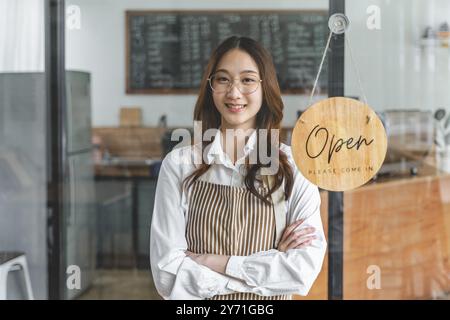 Glückliche junge Ladeninhaberin, die neben dem Open-Schild steht und lächelt Stockfoto