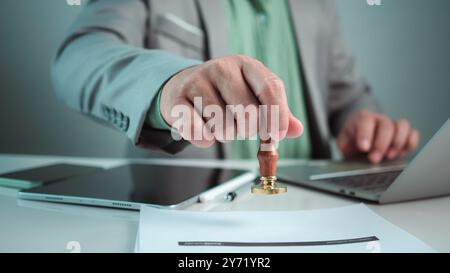 Geschäftsmann-Handstempel mit genehmigtem Stempel auf dem genehmigten Dokument am Schreibtisch, validiert und verwaltet Geschäftsdokumente und Vereinbarungen, Genehmigungsstatus Stockfoto