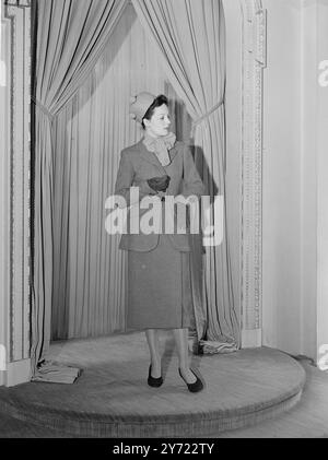 Tweeds In Wein. Dieser Anzug aus Tweed mit Fischgrätmuster in Rot und Wein hat einen geraden Rock und abgerundete Hüften in der Jacke. Es wird zu einem geraden, passenden Obermantel und einer roten Chiffonbluse getragen. Der zierliche Hut ist aus rotem Stroh. 28. Februar 1948 Stockfoto