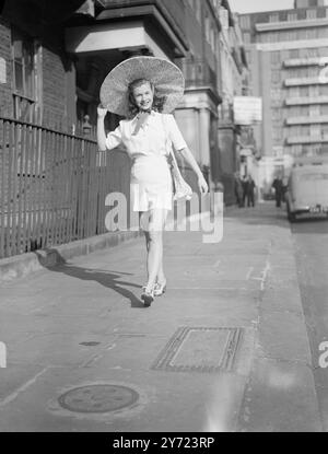 Für Die Sonne Geeignet. Die Londoner blicken neidisch auf die sonneneinladende Kleidung, die diese junge Dame heute auf dem Weg zu einer Modenschau trägt. Das warme Wetter überzeugte sie nicht nur, das Outfit auf der Show zu modellieren, sondern auch auf dem Weg dorthin. Ihr riesiger Bilderhut, ihre Handtasche und Krawattenschuhe waren in passendem Harlequin-Stoff. März 1948 Stockfoto