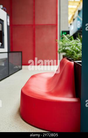 Vertikale Aufnahme des öffentlichen Bereichs im Business Center mit Grün und gemütlichen Designer-Sitzgelegenheiten in leuchtendem Rot. Loungebereich für Geschäftsleute, Kopierbereich Stockfoto