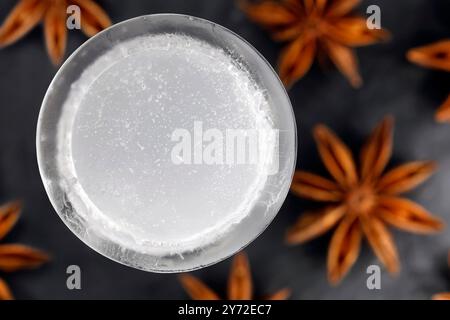 Blick von oben auf eisiges Ouzo, serviert in einem Eisglas, isoliert auf einer schwarzen Schieferplatte zwischen Sternanisfrüchten, Stockfoto