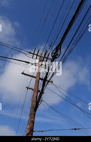 : Fotos mit Stromleitungen, Straßenecken und Autos mit klarem blauem Himmel und städtischer Infrastruktur im Hintergrund. Stockfoto