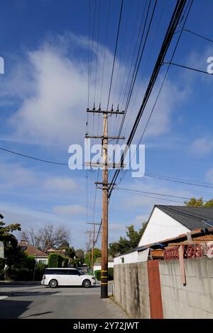 : Fotos mit Stromleitungen, Straßenecken und Autos mit klarem blauem Himmel und städtischer Infrastruktur im Hintergrund. Stockfoto