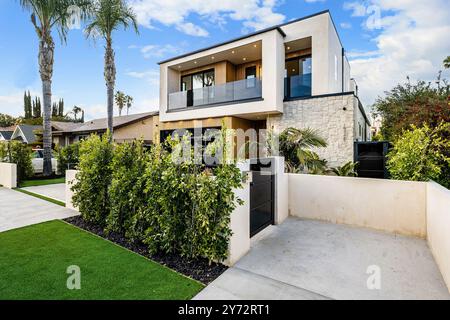 Modernes zweistöckiges Haus mit einem sauberen und minimalistischen Design, mit einem Vorhof mit üppigem Grün und Palmen unter blauem Himmel. Stockfoto